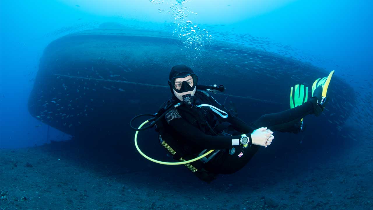 A diver exploring the El Peñon shipwreck in Tabaiba, Tenerife, during a dive with LoCura Diving, with the wreck visible in the background