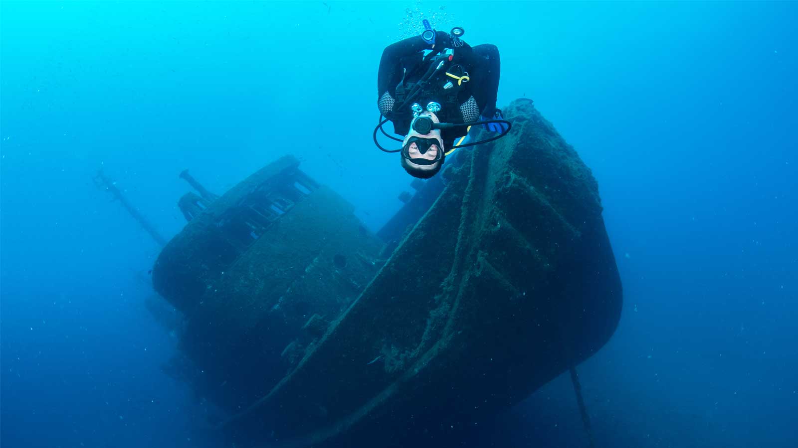 Diver swimming with the El Peñón shipwreck in Tabaiba in the background during a dive with LoCura Diving.