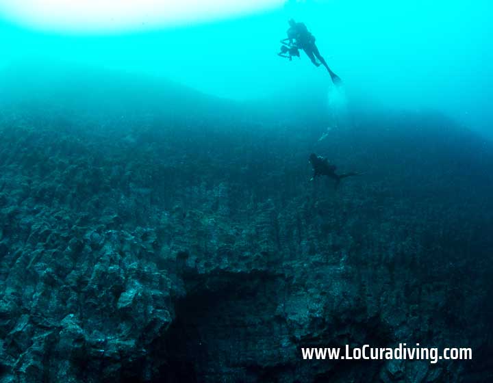 Two divers exploring the prismatic rock formations of La Rapadura dive site in Tenerife.