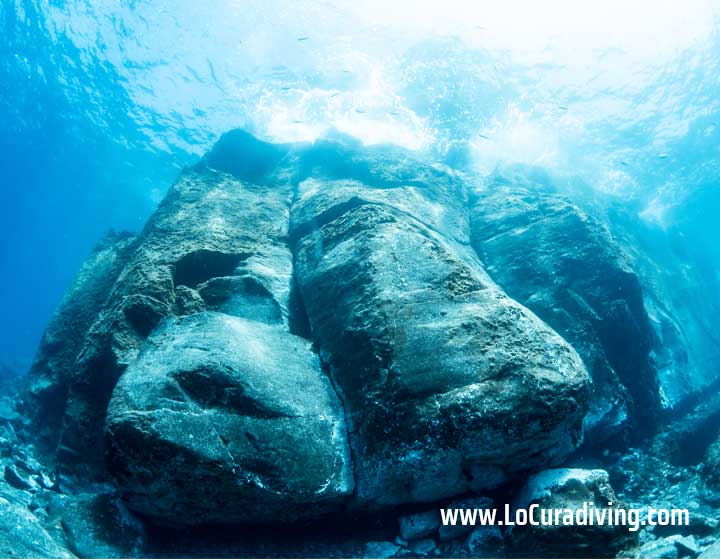 Massive stone wall in shallow waters at El Balito, leading to the first cavern.